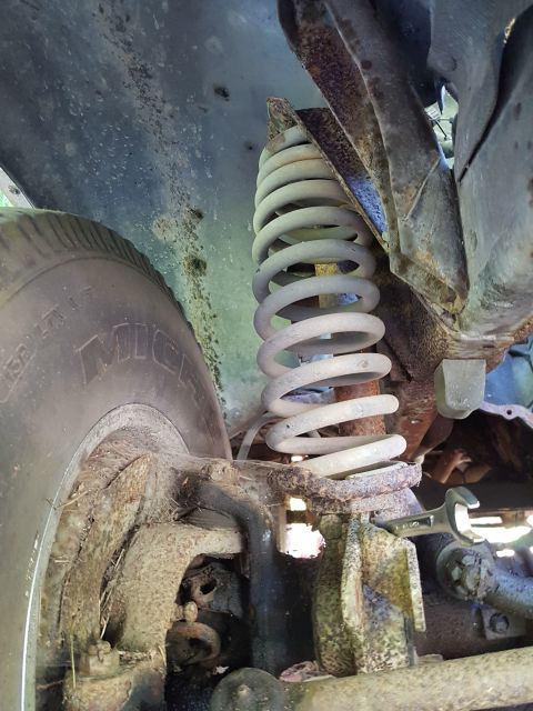1978 Ford Bronco - This image shows the suspension system of a vehicle, including a coil spring and part of a tire. The components appear rusty.