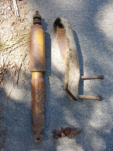 1978 Ford Bronco - A rusty yellow shock absorber and a metal bracket with bolts are displayed on an asphalt surface.