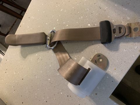 1996 Ford Bronco - A tan seatbelt assembly is shown laid out on a countertop, detached from a vehicle.