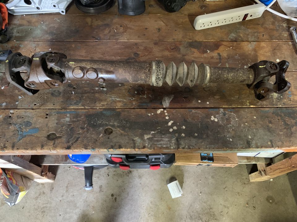 Driveshaft with U-joints and a rubber boot, resting on a wooden workbench
