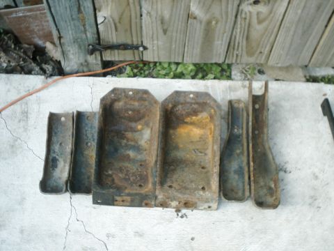 1984 Ford Bronco - A collection of rusty metal parts, possibly for a vehicle, are displayed on a concrete surface against a wooden fence.