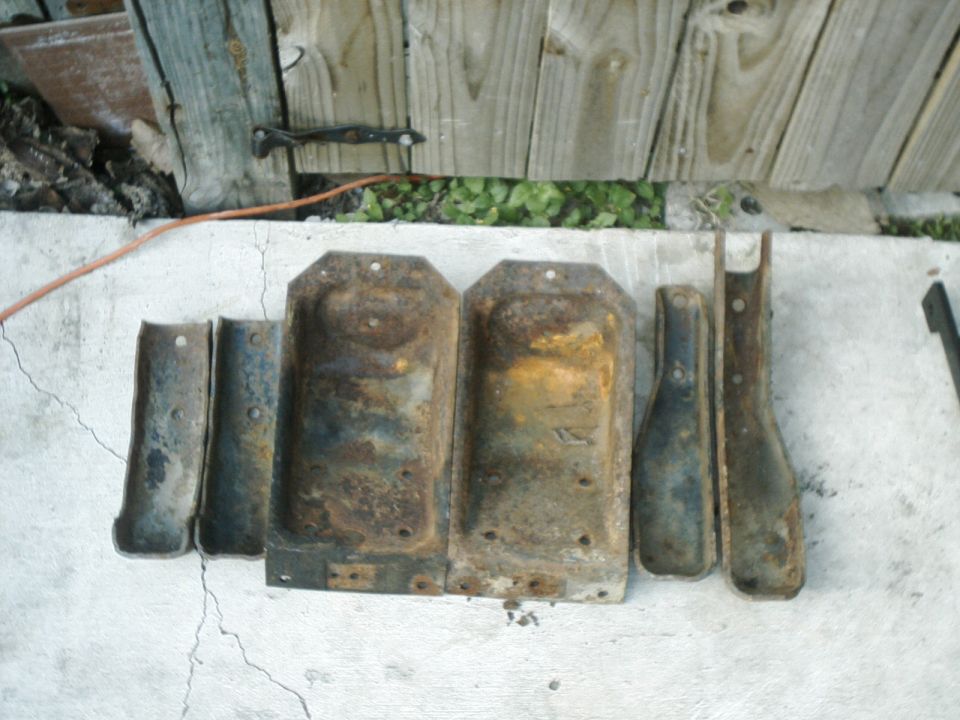 Several rusty metal brackets and plates laid out on concrete