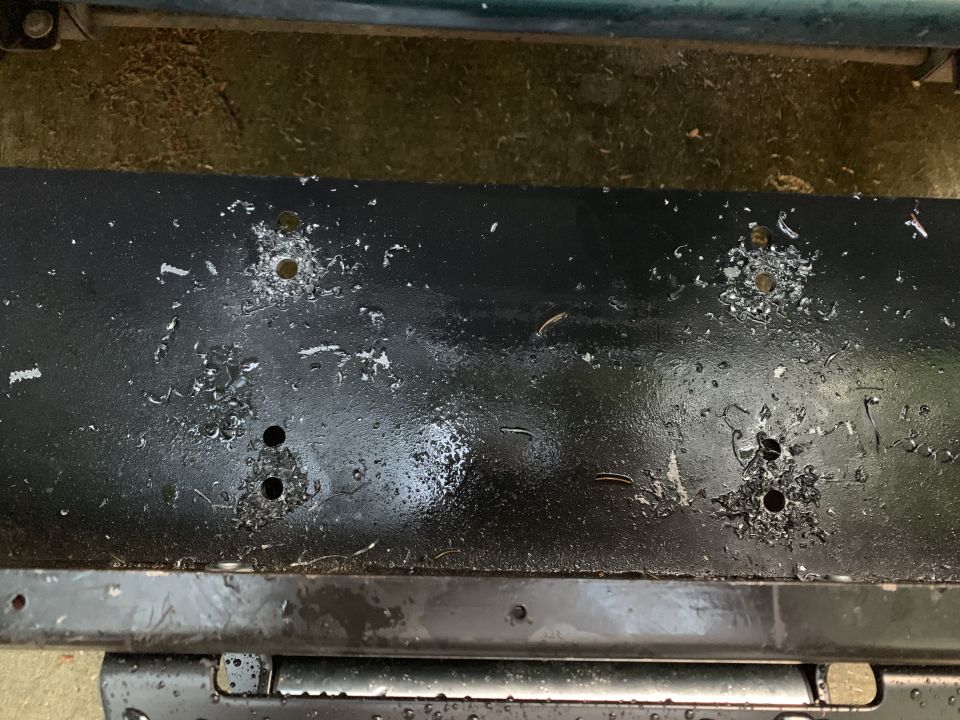 Close-up of a black metal vehicle frame with several holes and chipped paint