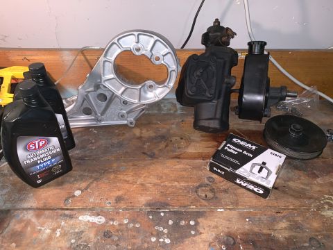 1996 Ford Bronco - Various automotive parts are laid out on a workbench, including a power steering pump and associated components.