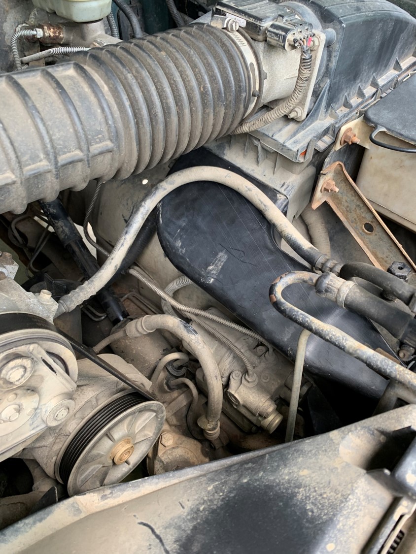 Close-up of engine compartment with air intake hose and various hoses and pulleys visible