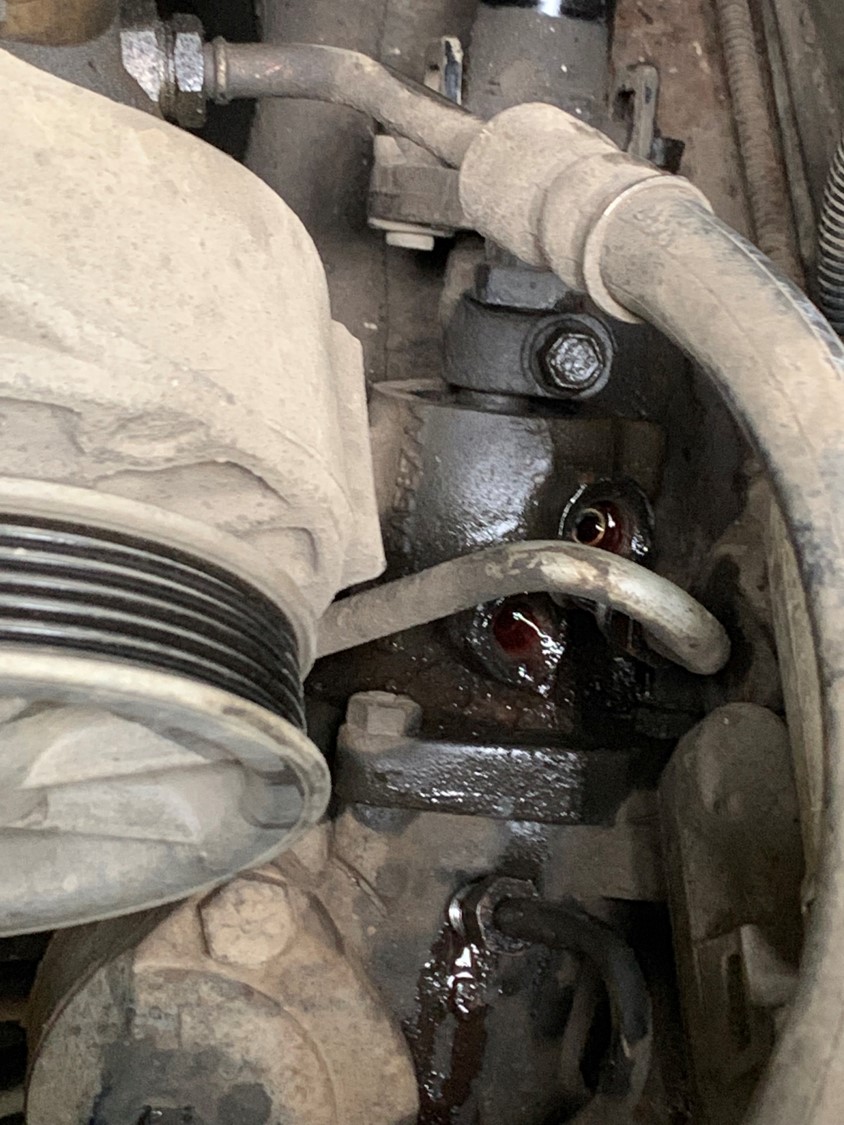 Engine component with dark fluid leaking from a fitting, showing hoses and metal parts