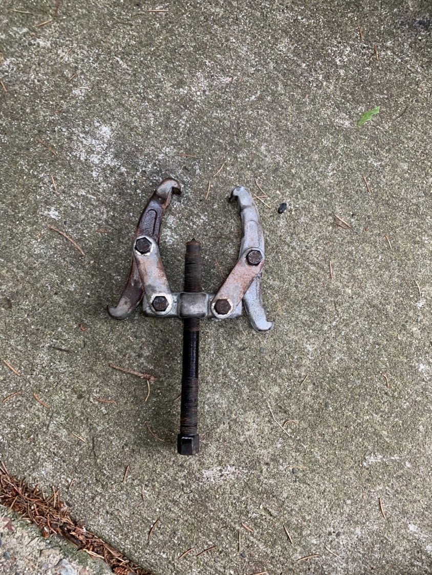 Gear puller tool on concrete ground. The tool has a central screw and two adjustable arms