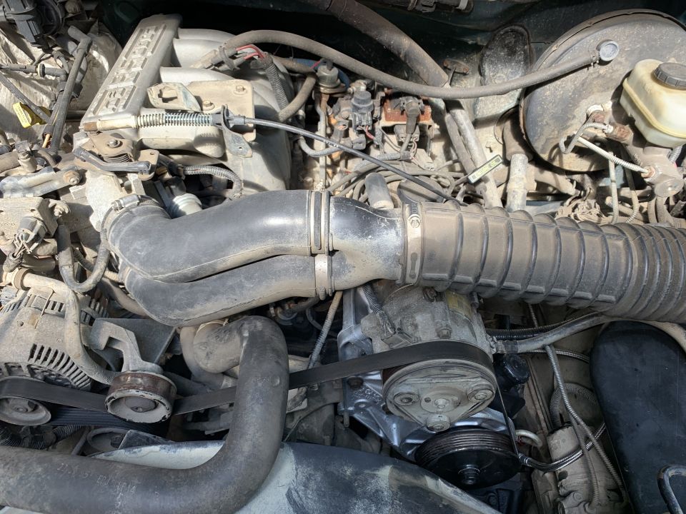Engine bay with hoses, belts, and engine components visible. Some dust and grime present