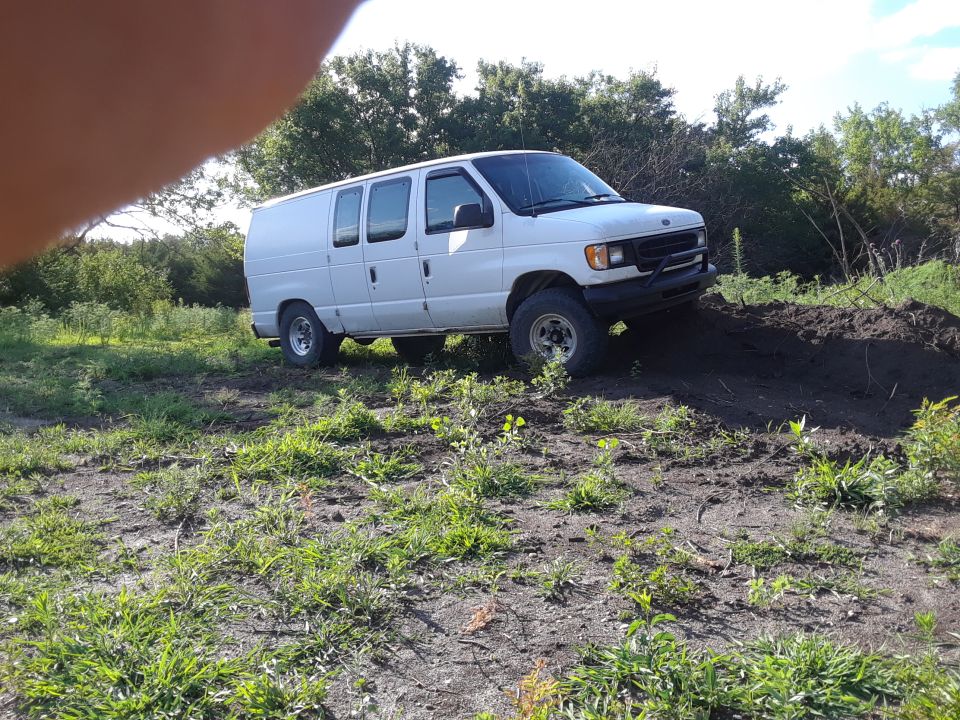 White van on dirt mound, front 3/4 view. Visible text: SUPER MOTORS www.supermotors.net