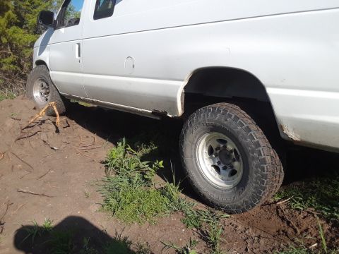 1999 Ford E250 - This white van, likely a 1999 Ford E250, is shown from the side with off-road tires on a dirt path.