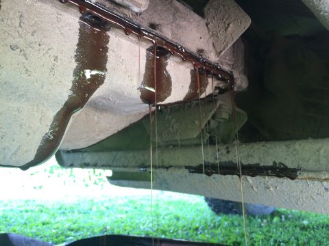 1993 Ford Bronco - Dark oil is leaking from the underside of a vehicle, dripping onto the ground.