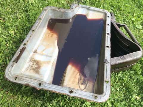 1993 Ford Bronco - An oil pan, likely from a Ford vehicle, sits on grass with dark fluid inside.