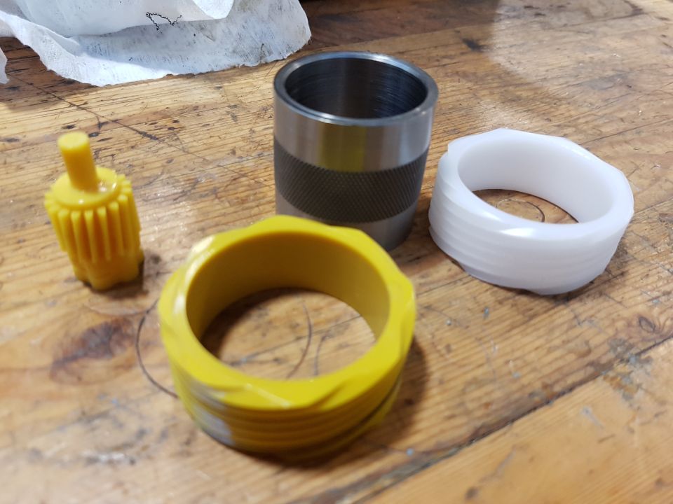 Various mechanical parts including yellow and white plastic pieces and a metal cylinder on a wooden surface.