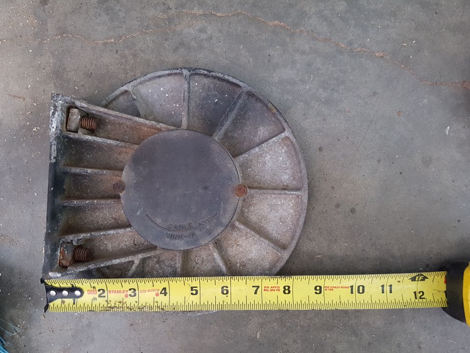 Metal pulley or winch part with radial fins and a central plate, measured with a tape measure.