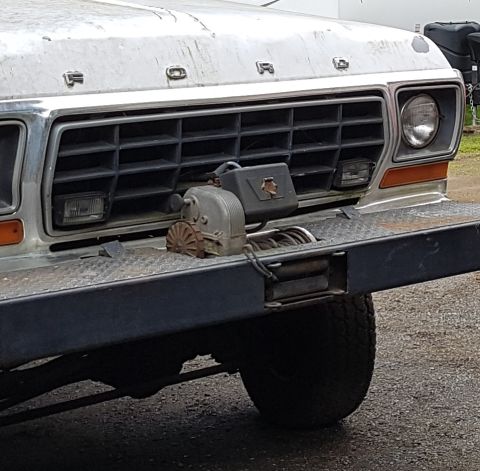 1978 Ford Bronco - The front grille and bumper of a weathered, older model Ford truck are shown. A winch and a small toolbox are mounted on the front bumper.