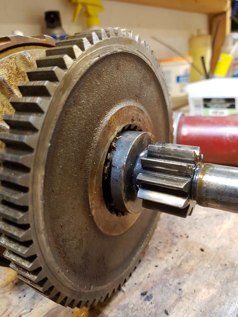 1978 Ford Bronco - A close-up, slightly angled view of a large metal gear with teeth, attached to a shaft with smaller gears. The metal appears worn and greas…