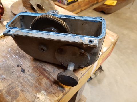 1978 Ford Bronco - A close-up, high-angle view of an open metal housing with a gear inside, resting on a wooden workbench. The housing has a blue sealant arou…