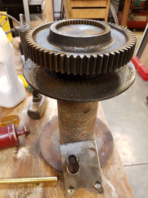 1978 Ford Bronco - A close-up view of a large, rusty metal spool with a heavy gear on top, resting on a wooden surface amongst various tools and metal parts.