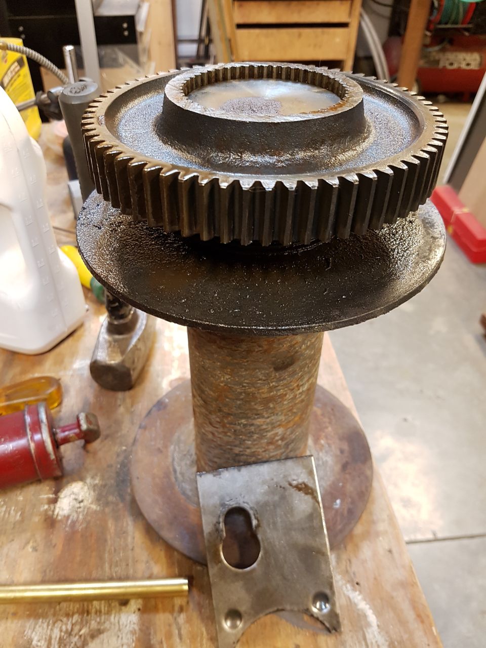 Rusty metal spool with a large gear on top, surrounded by tools.