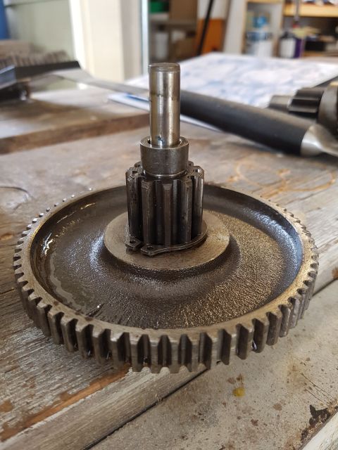 1978 Ford Bronco - A close-up view of a metal gear assembly with a shaft on a wooden surface. The gear is oily and shows signs of wear.