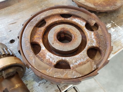 1978 Ford Bronco - A close-up, overhead view of a rusty, circular metal part with a toothed outer edge and a central hub. The part is resting on a weathered w…