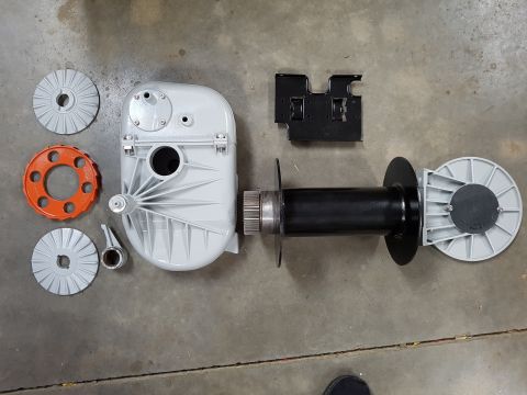1978 Ford Bronco - A collection of disassembled parts for what appears to be a gearbox and winch assembly is laid out on a concrete floor. Visible components…
