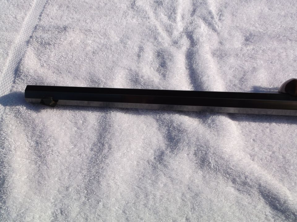 Close-up of a dark-colored firearm barrel resting on a white towel. A SuperMotors logo is visible in the lower right corner