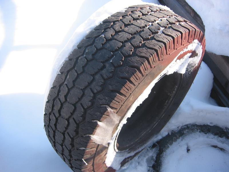 Used all-season truck tire lying in snow, tread and rusty sidewall in close-up