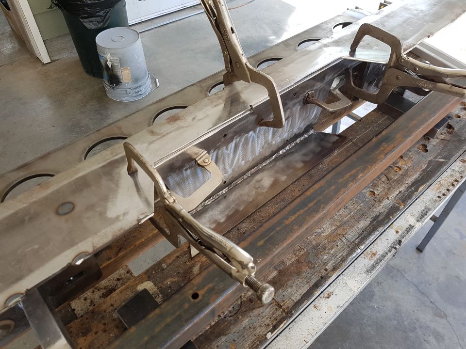 Metal frame section held by clamps, showing welding marks