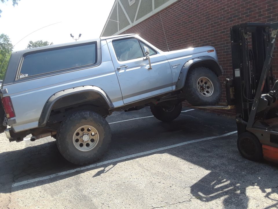 Light blue Ford Bronco with aftermarket wheels and fender flares being lifted by a forklift