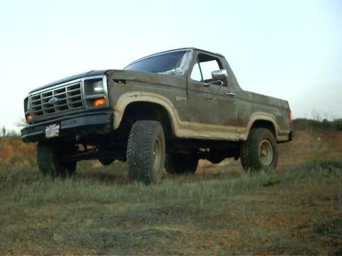 1985 Ford Bronco - This weathered 1980s Ford Bronco is seen from a 3/4 front angle on a grassy incline.