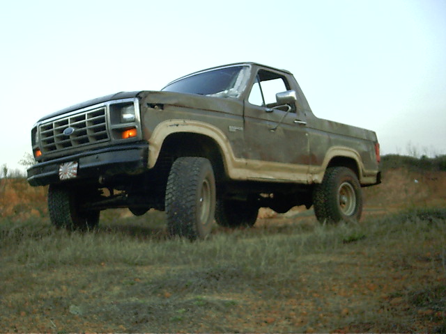 Brown 1980s Ford Bronco with a dented front end parked on a grassy hill