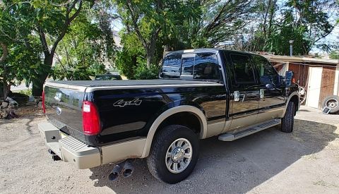 2010 Ford F-250 - This black Ford Super Duty pickup truck is parked in a gravel lot with trees and a building in the background.