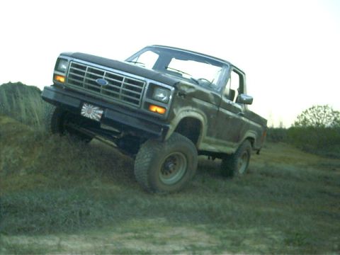 1985 Ford Bronco - This Ford truck is shown off-road, climbing a dirt and grass incline.