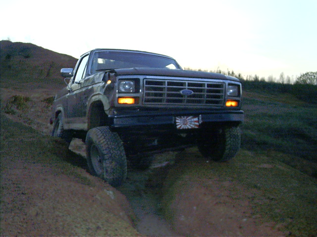 Dark 1985 Ford Bronco driving off-road on a dirt hill