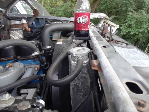 1985 Ford Bronco - A Dr. Pepper bottle rests on the radiator of an engine bay, obscuring some of the mechanical components.