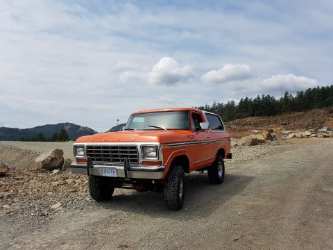 1978 Ford Bronco - This 1978 Ford Bronco is captured from a three-quarter front angle, showing its distinctive grille and orange paintwork against a cloudy sk…