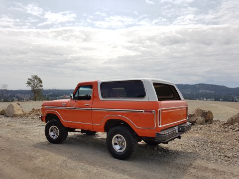 1978 Ford Bronco - This 1978 Ford Bronco is captured from a three-quarter front view, its distinctive orange and white paint scheme against a cloudy sky.
