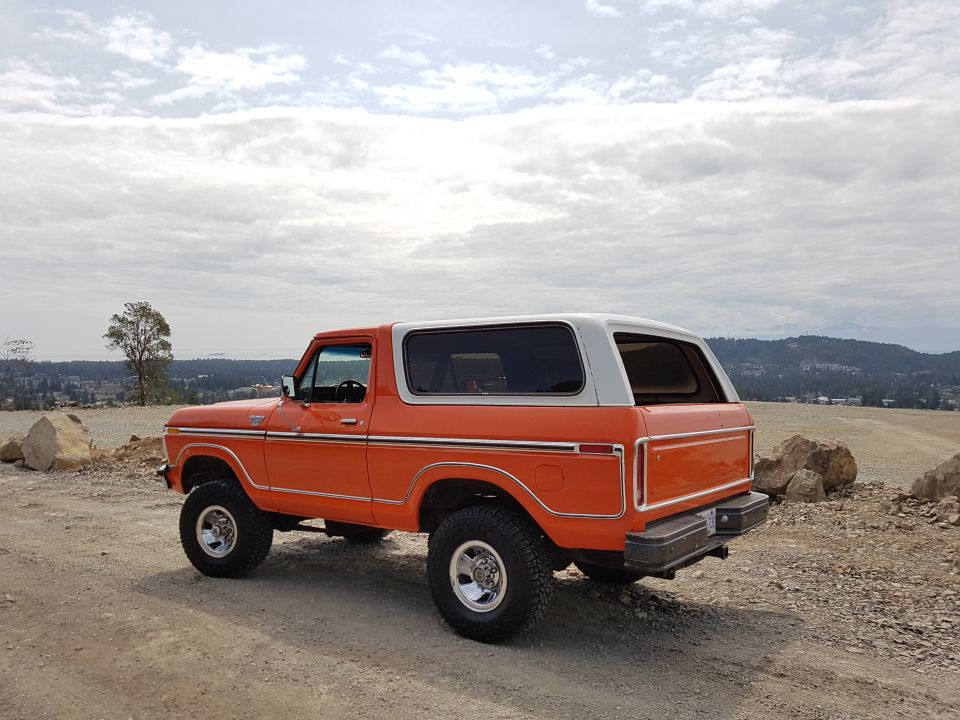 Orange and white 1978 Ford Bronco parked on a dirt road with a scenic overlook