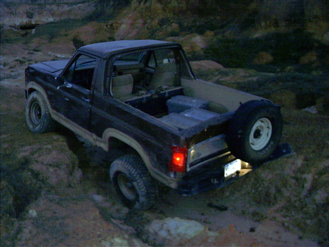 1985 Ford Bronco driving off-road, rear view with spare tire mounted