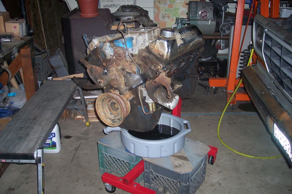 Engine on an engine stand with a drain pan underneath, next to a vehicle's front end