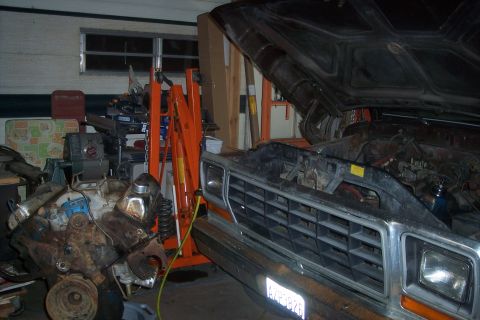 1978 Ford Bronco - A 1978 Ford Bronco sits in a garage with its hood open, and a separate engine is visible nearby, possibly for repair or replacement.