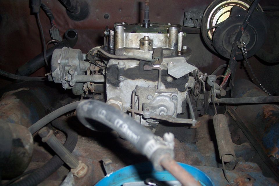 Close-up of a carburetor with hoses and wiring in an engine bay