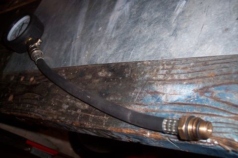 1995 Ford Bronco - A close-up of a pressure gauge and its connected hose, placed on a weathered wooden surface.