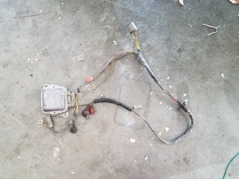 1985 Ford Bronco - A close-up view of an automotive wiring harness and voltage regulator lying on a concrete surface.