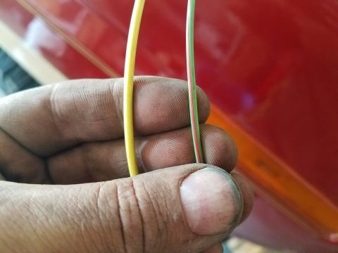 1985 Ford Bronco - Close-up of a hand holding electrical wires against the red exterior of a vehicle.