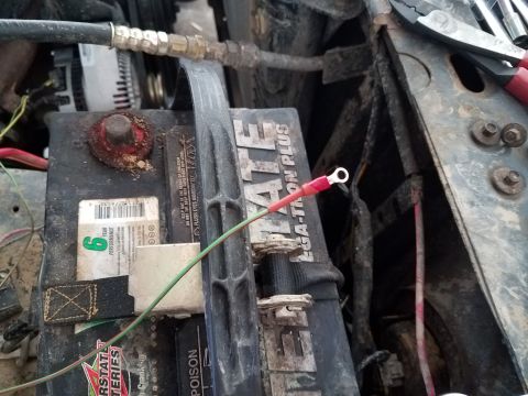 1985 Ford Bronco - Close-up of a car battery with wiring and tools in the engine bay.