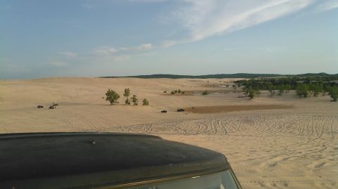 1978 Ford Bronco - A 1978 Ford Bronco navigates a sandy terrain with other vehicles visible in the distance under a partly cloudy sky.