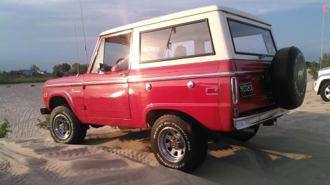 1978 Ford Bronco - A red and white 1978 Ford Bronco is parked on a sandy dune, with another vehicle visible in the background.