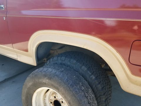 1985 Ford Bronco - Close-up of the rear fender and wheel area of a maroon SUV with tan trim.